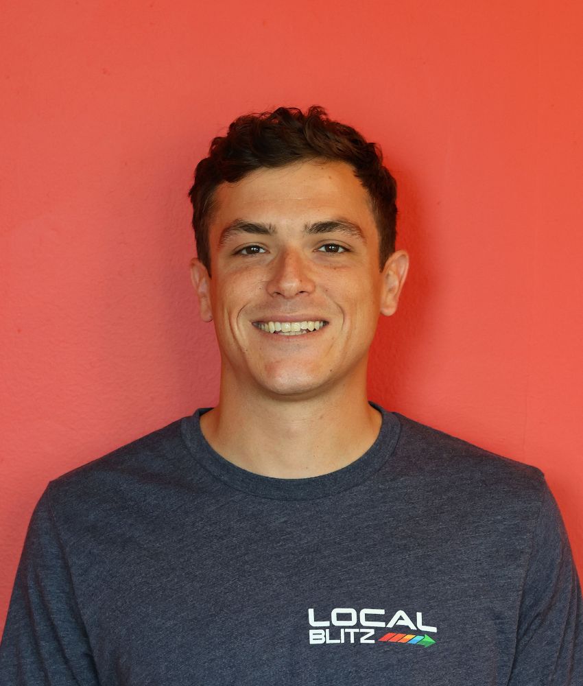 Smiling person in Local Blitz shirt against red background.